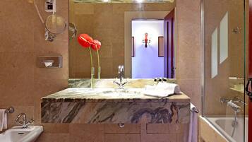 A bathroom with a marble sink, a mirror, a red flower arrangement, and a glass shower enclosure.