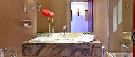 Un baño con lavamanos de mármol, un espejo, un arreglo floral rojo y una cabina de ducha de vidrio.