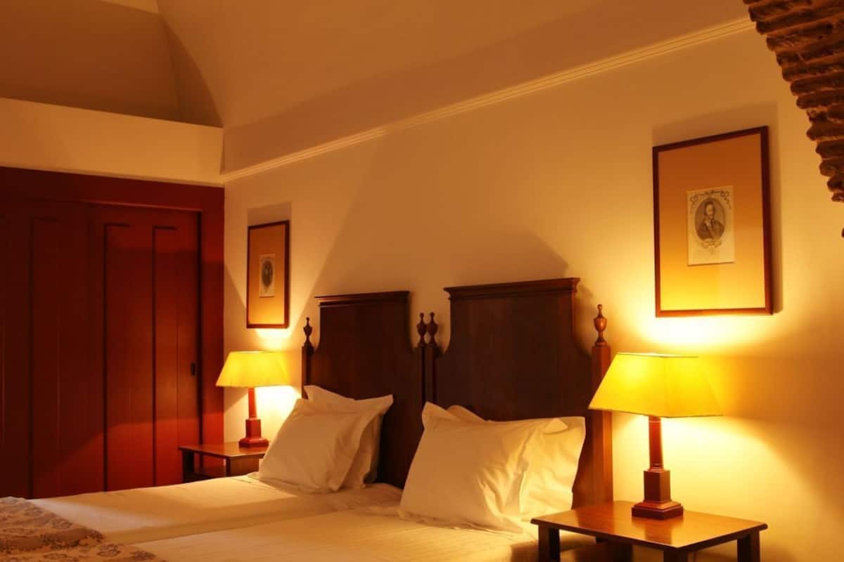 A bedroom with a bed, two bedside tables with lamps, a wooden wardrobe, and a framed picture on the wall.