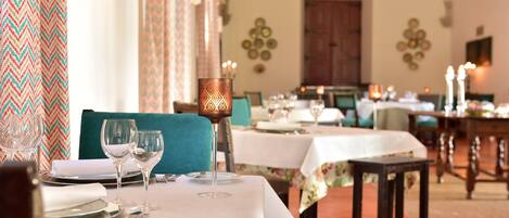 Un comedor con mesas dispuestas para una comida, incluyendo copas de vino y cubiertos.