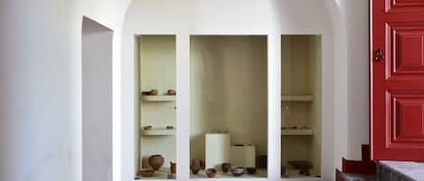 Un pasillo con puerta roja, paredes blancas y piso de baldosas.