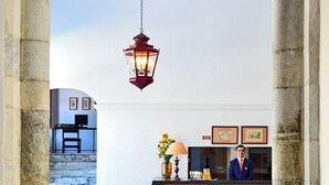 A hotel reception area with marble flooring, a wooden reception desk, a hanging lantern, and a staircase leading to another room.