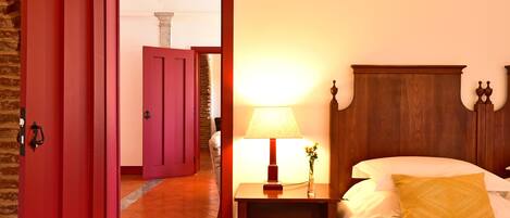 Une chambre d’hôtel avec une tête de lit en bois, une table de chevet avec une lampe et un lit avec un seul oreiller jaune.