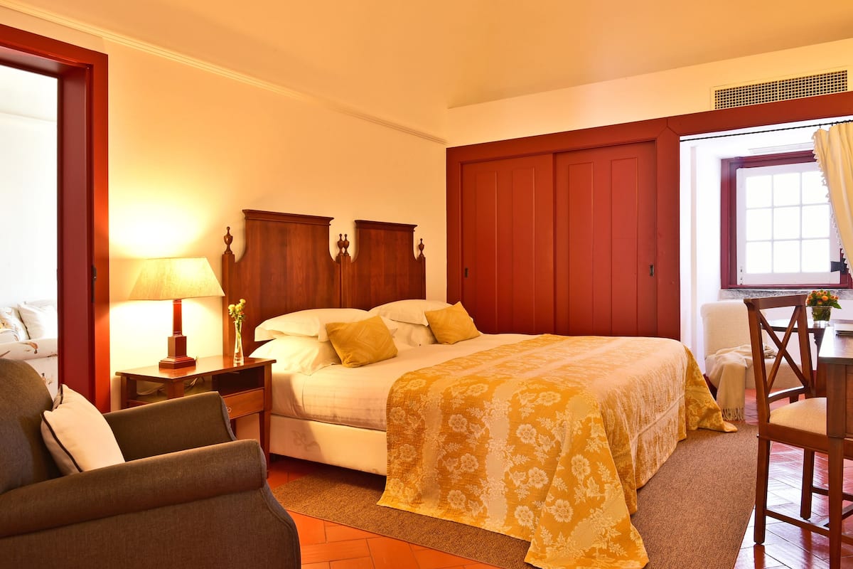 A hotel room with a bed, a desk, a chair, and a lamp.