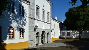 A historic building with arched windows and a yellow base, featuring a paved courtyard and a clear sky.