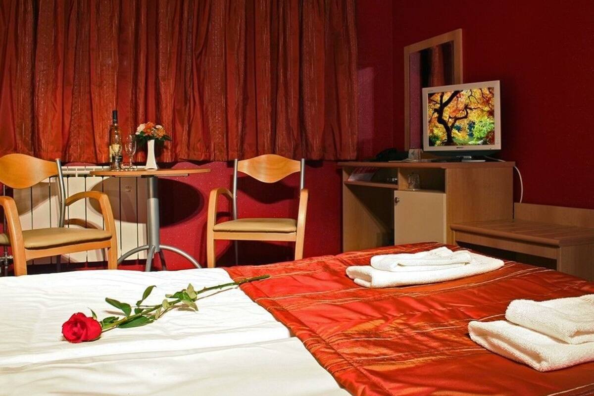 A hotel room with a bed, a desk, two chairs, a television, and a red curtain.