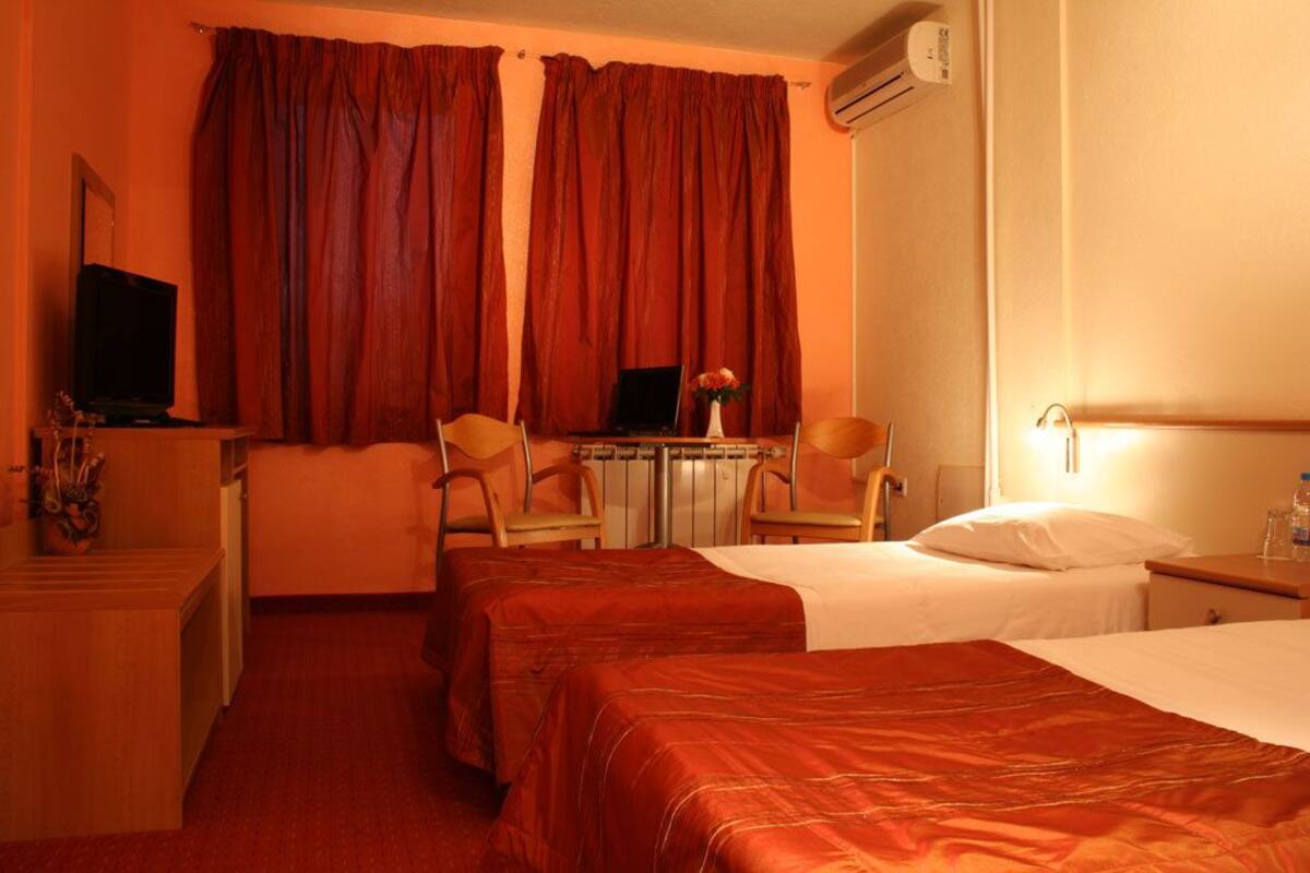 A hotel room with two beds, a desk with a laptop, a chair, and an air conditioning unit.