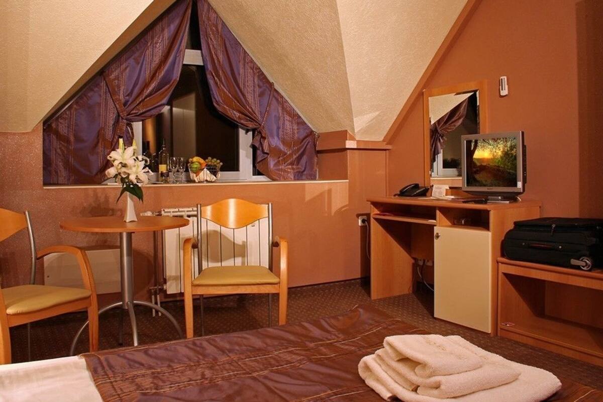 A compact hotel room with a bed, a desk, a chair, a television, and a window with curtains.