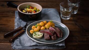 A plate of food with steak and potatoes, a bowl of salad, and a knife on a wooden table.