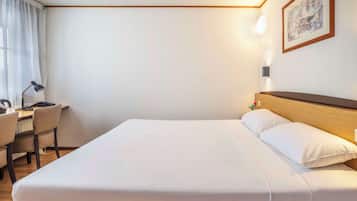 A hotel room with a bed, a desk, a chair, and a nightstand.