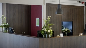 Un comptoir d’accueil avec un panneau en bois en arrière-plan, un mur d’accent rouge et un luminaire suspendu.