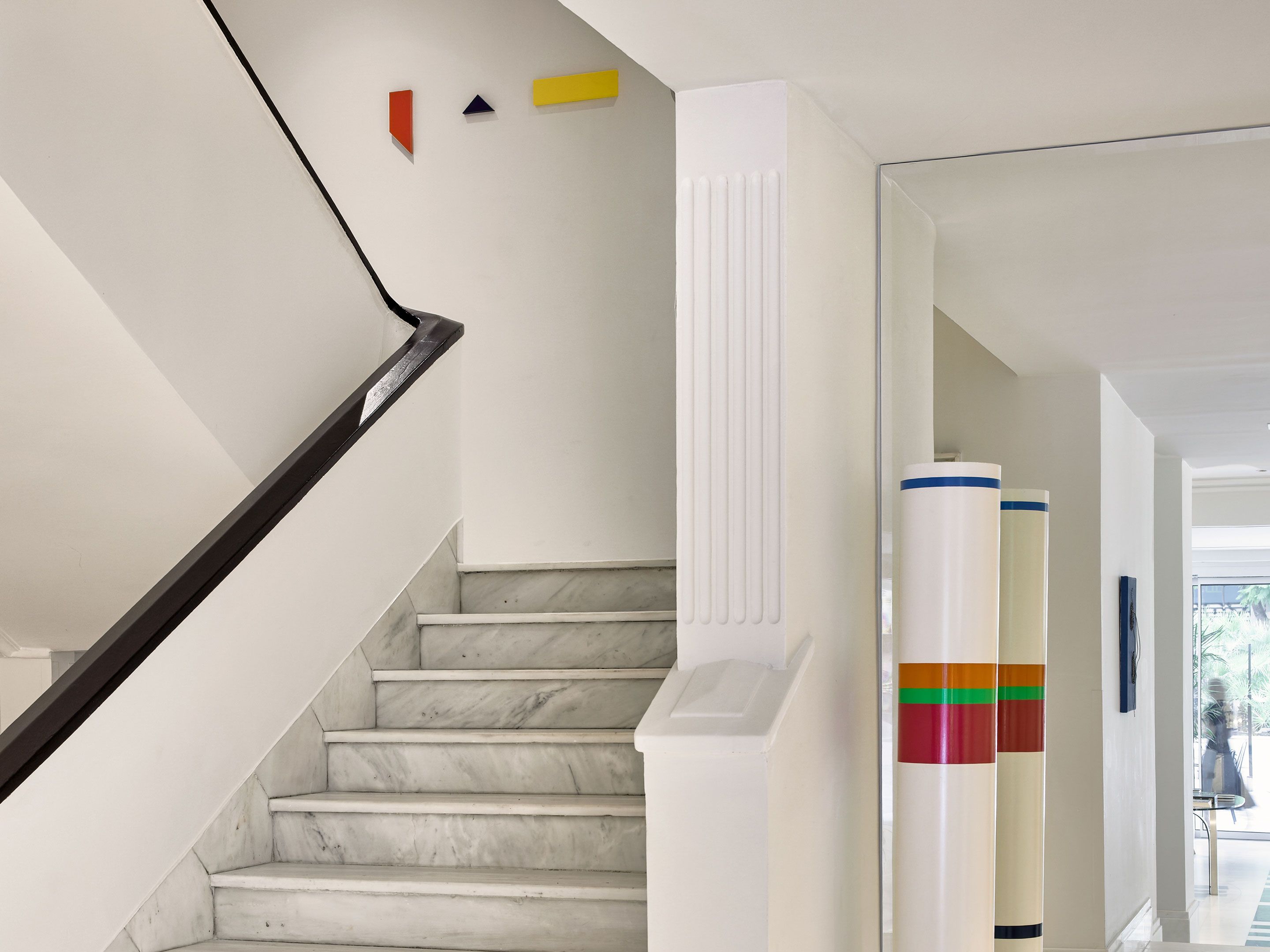 A staircase with marble steps and a black handrail, leading to a landing with a white wall and a radiator.