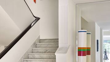 A staircase with marble steps and a black handrail, leading to a landing with a white wall and a radiator.