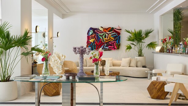A modern living room with a glass coffee table, white sofas, and a colorful abstract painting on the wall.
