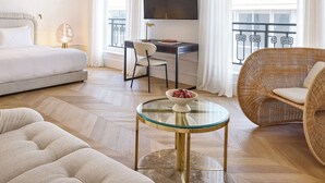 A modern hotel room with a bed, a desk with a TV, a wicker chair, and a glass coffee table. - ATHENA Pallas (Athens)