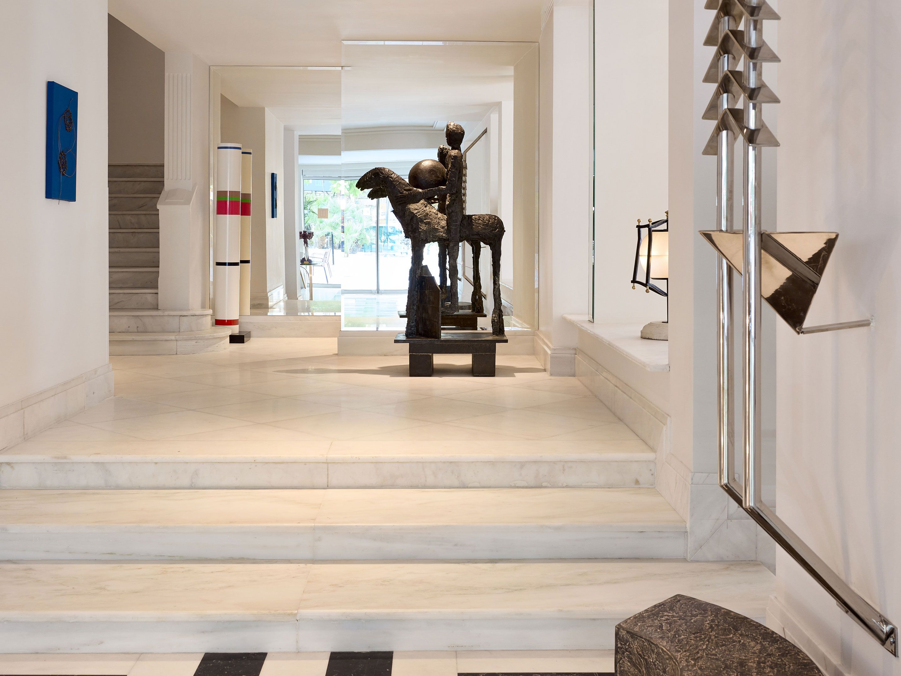 A hallway with marble flooring, a sculpture, and a staircase.