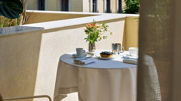 Un tavolo da balcone con una tovaglia bianca, un piccolo vaso con fiori, un piatto con una pasticceria e una tazza.