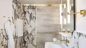 A bathroom with a marble wall, a white sink, a gold-framed mirror, and a towel rack. - ATHENA Pallas (Athens)