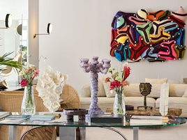 Uma sala de estar moderna com uma mesa de centro de vidro, vasos decorativos e um quadro abstrato colorido na parede.