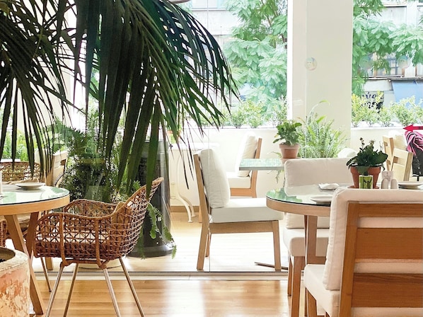 A cozy indoor seating area with wicker chairs, a round table, and potted plants. - ATHENA, A Hotel to Live (Athens)