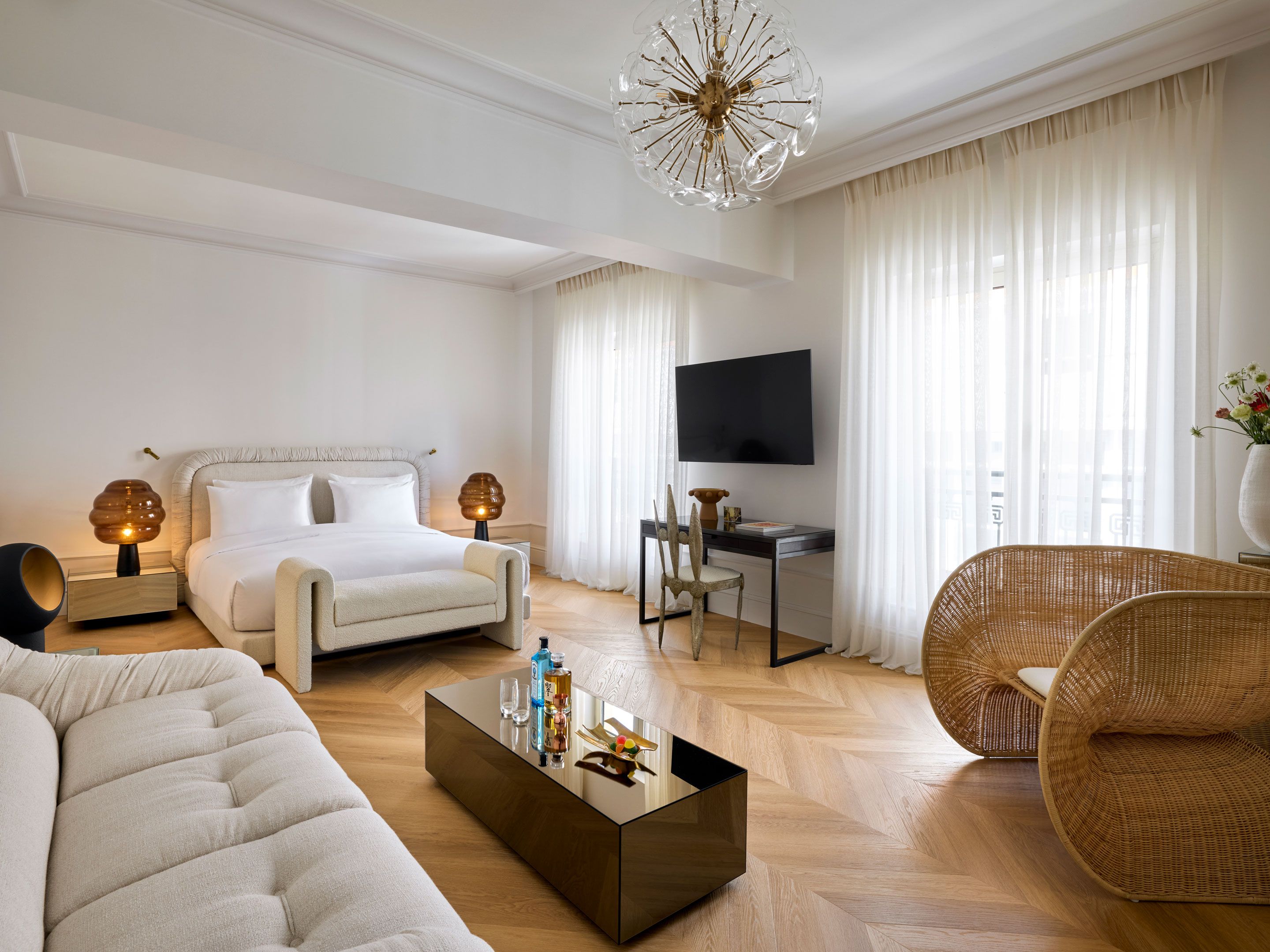 A modern hotel room with a bed, a desk, a television, a sofa, and a coffee table.
