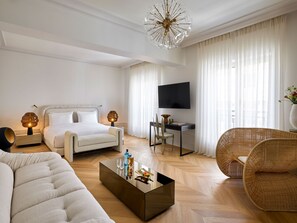 A modern hotel room with a bed, a desk, a television, a sofa, and a coffee table. - ATHENA Pallas (Athens)