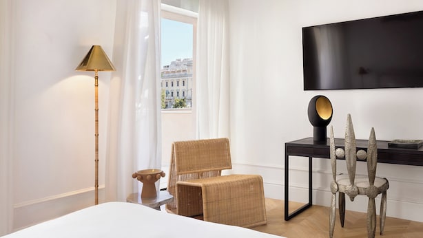 A hotel room with a bed, a desk with a chair, a lamp, and a TV on the wall. - ATHENA Pallas (Athens)