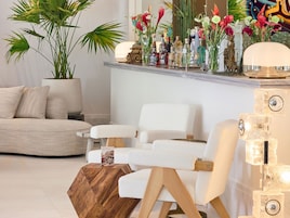 Uma sala de estar moderna com sofá, poltronas, mesa de centro, planta em vaso e prateleira com objetos decorativos.