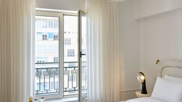 A hotel room with a bed, a nightstand, a table with drinks, and a view of the city through a balcony door.