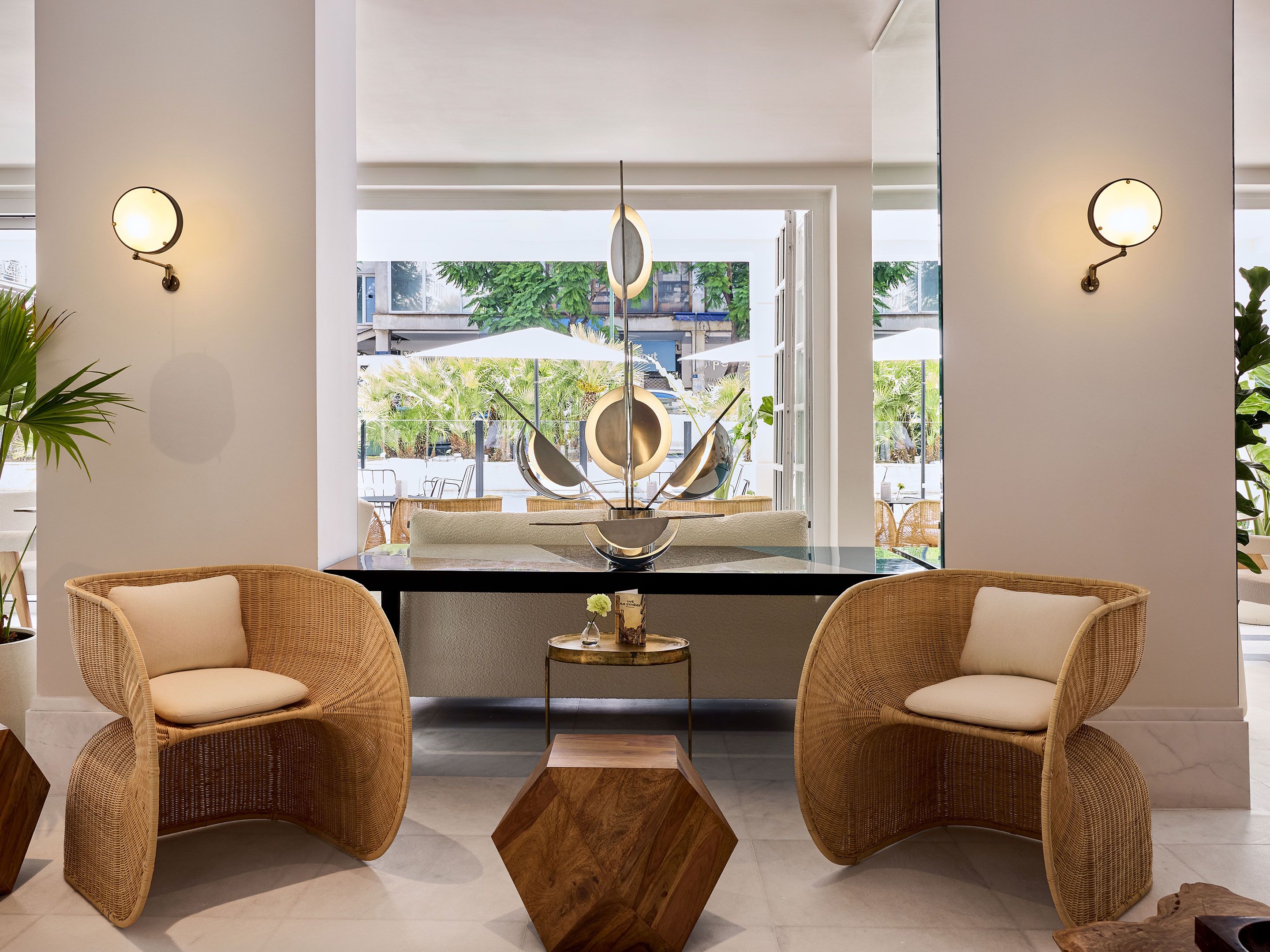 A modern interior with wicker chairs, a central table, and wall-mounted lights.