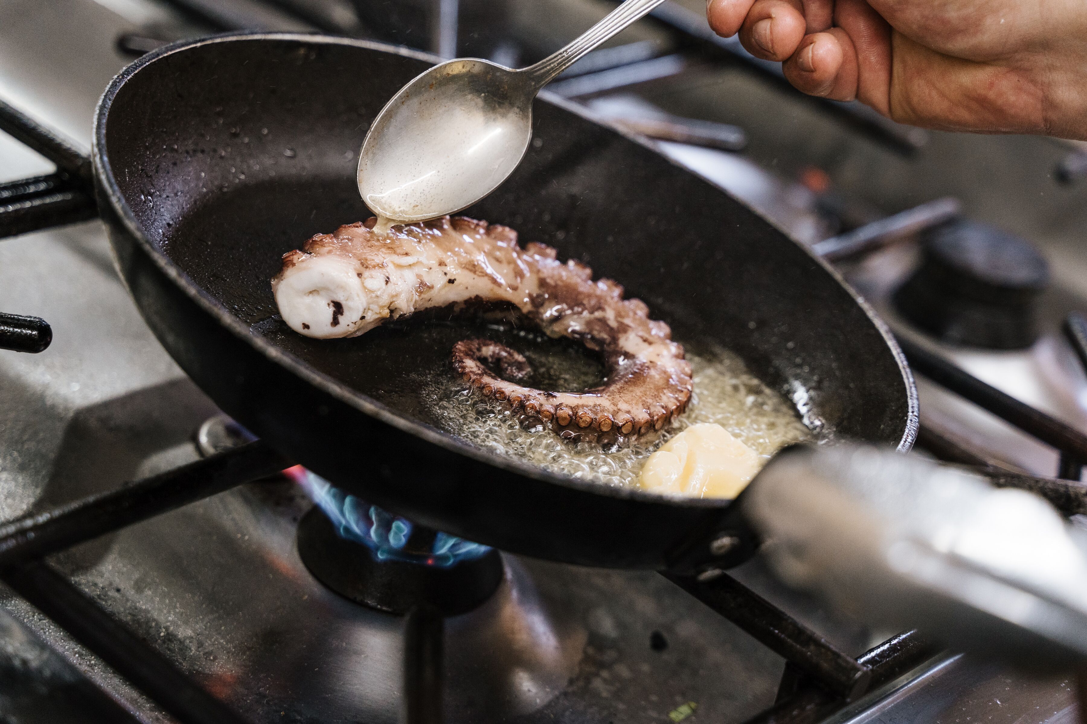 Ein Nahblick auf eine Bratpfanne auf einem Herd, in der ein Stück Oktopus gebraten wird.