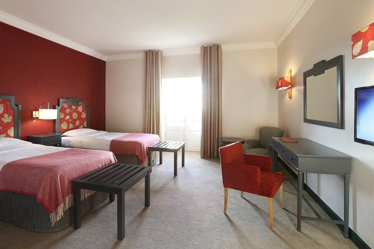 Habitación de hotel con dos camas, un escritorio, una silla y un televisor.
