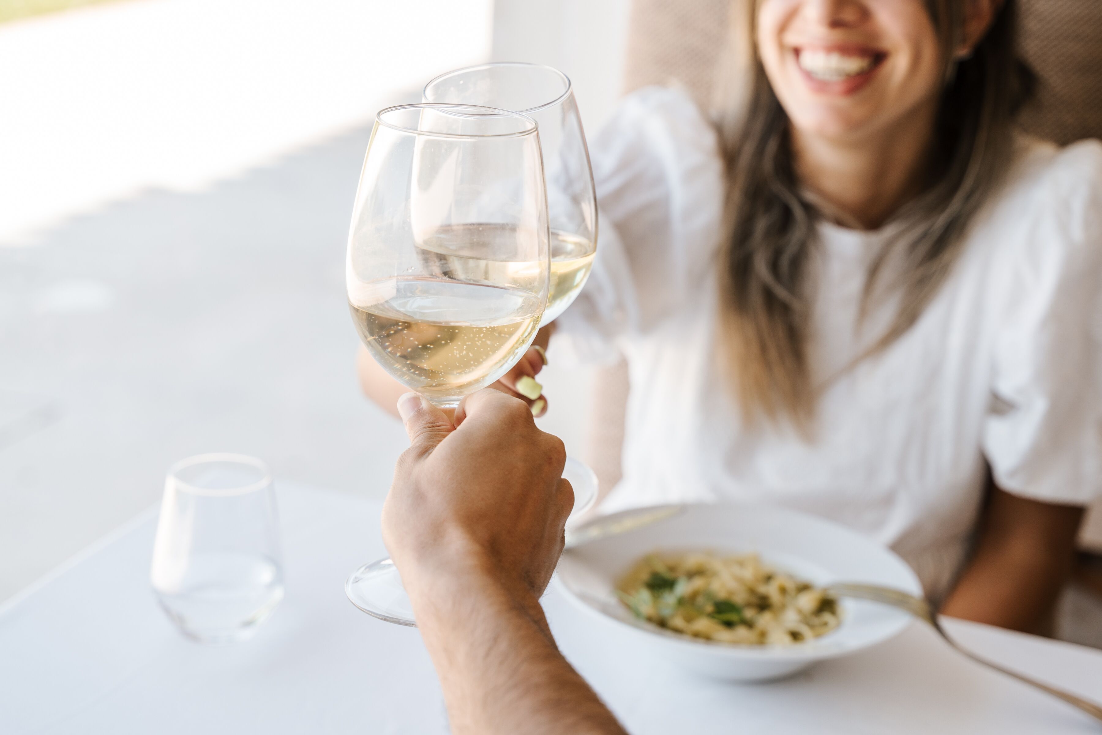 A dining table with a plate of food and a glass of white wine.