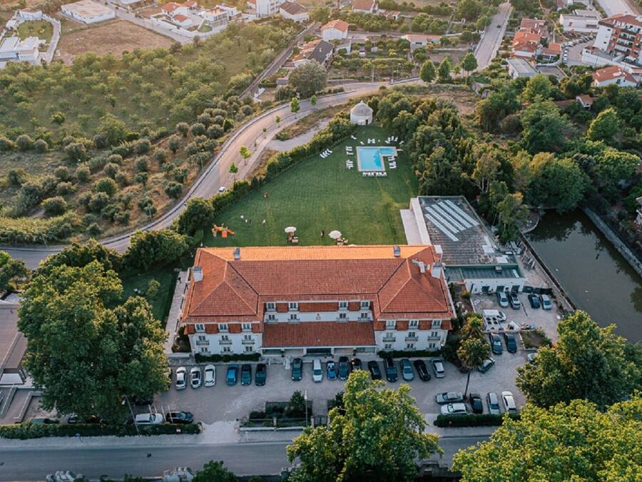An aerial view of a hotel with a swimming pool, parking area, and a river nearby.