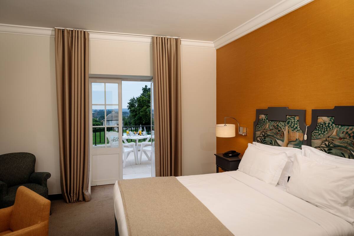 Habitación de hotel con cama, una silla, mesita de noche y vistas al exterior.