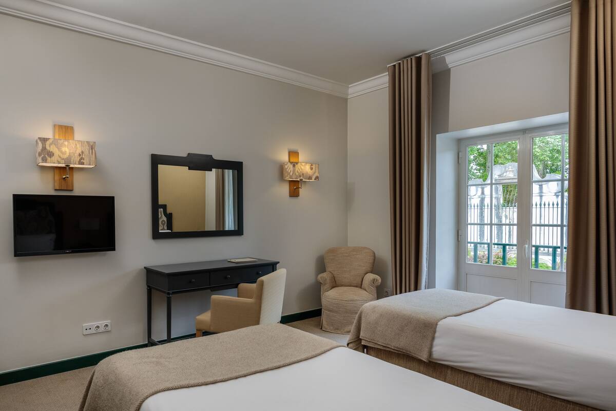 Habitación de hotel con dos camas, un escritorio, una silla, un televisor y dos lámparas fijadas a la pared.