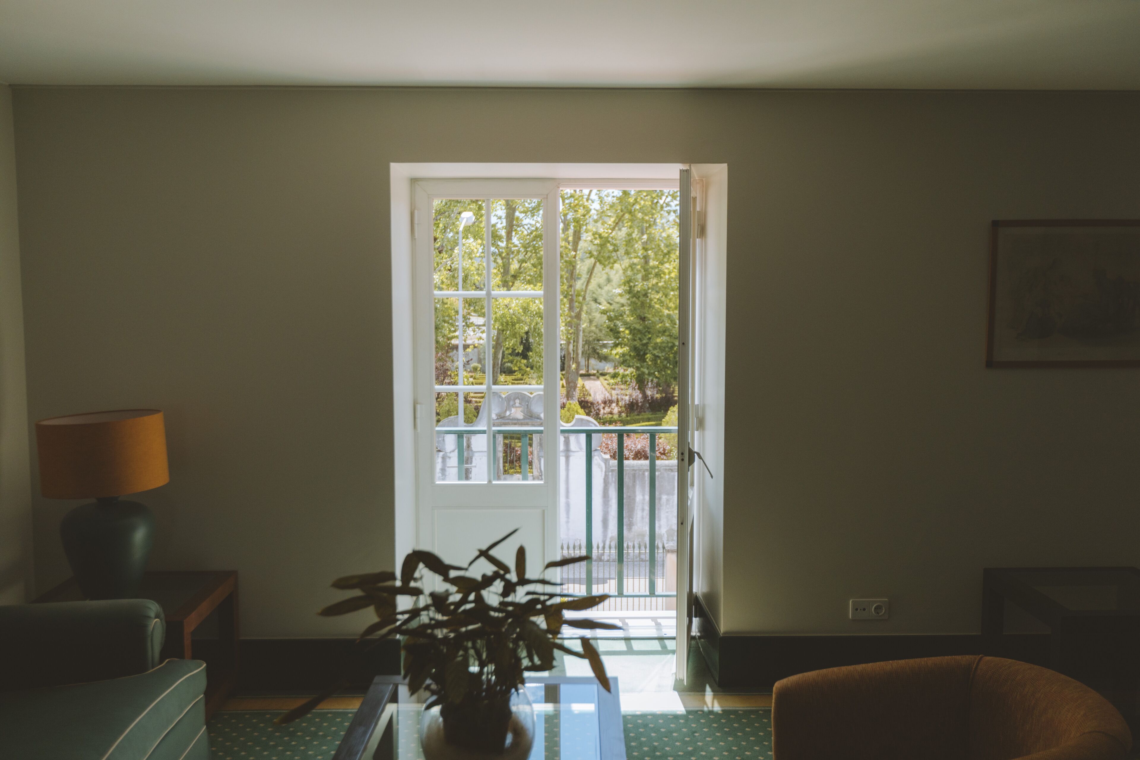 Habitación con sofá verde, una mesa con una planta, una lámpara y vistas a un balcón con barandilla a través de una puerta.