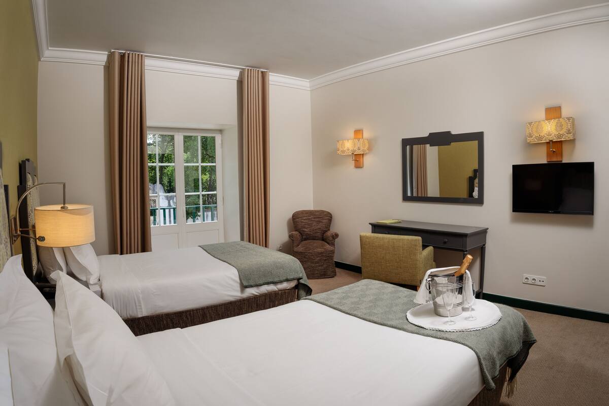 Habitación de hotel con dos camas, un escritorio, una silla, un televisor y una ventana con cortinas.