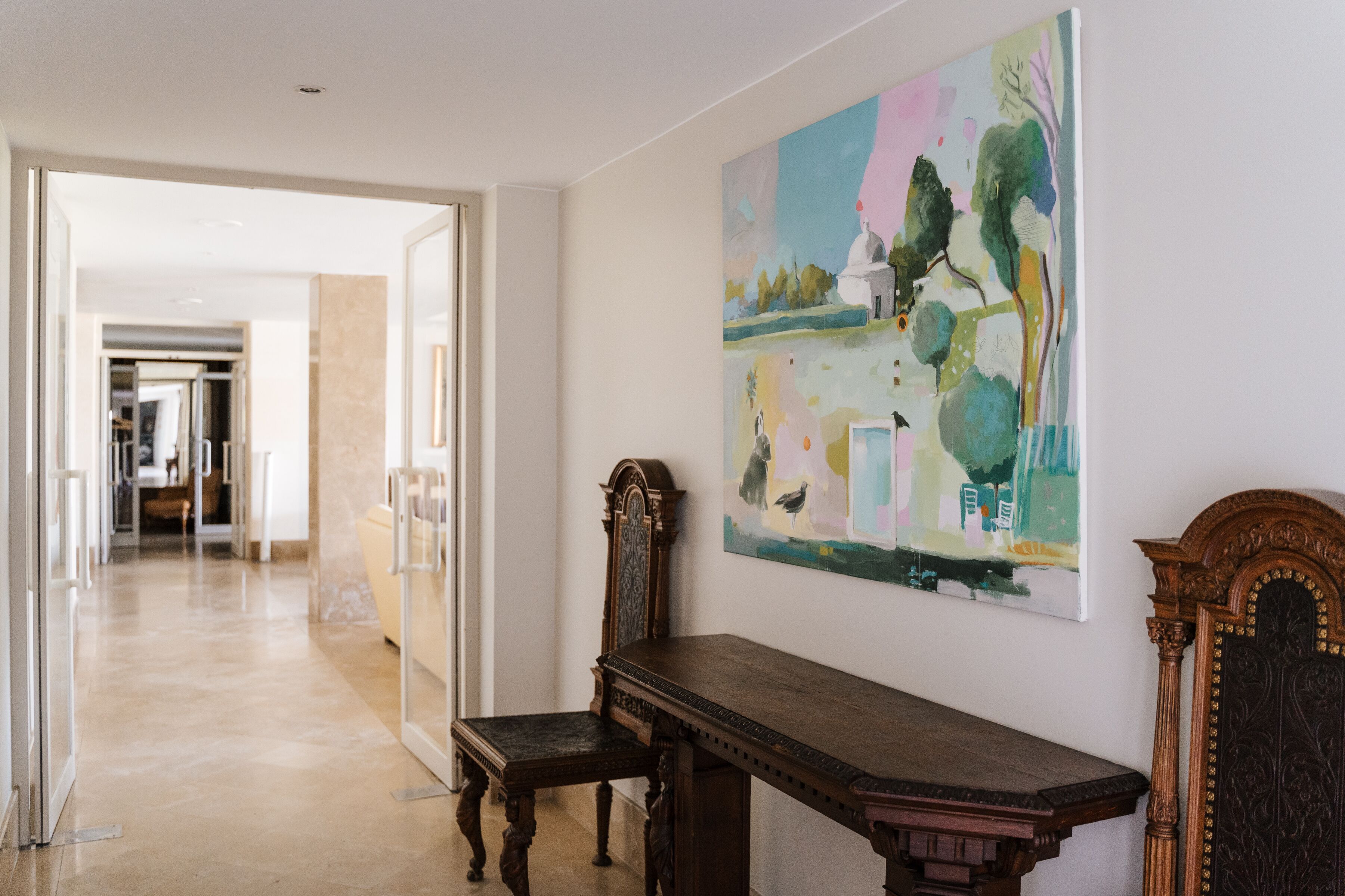 Un pasillo con un banco de madera, un cuadro en la pared y una puerta que da a otra habitación.