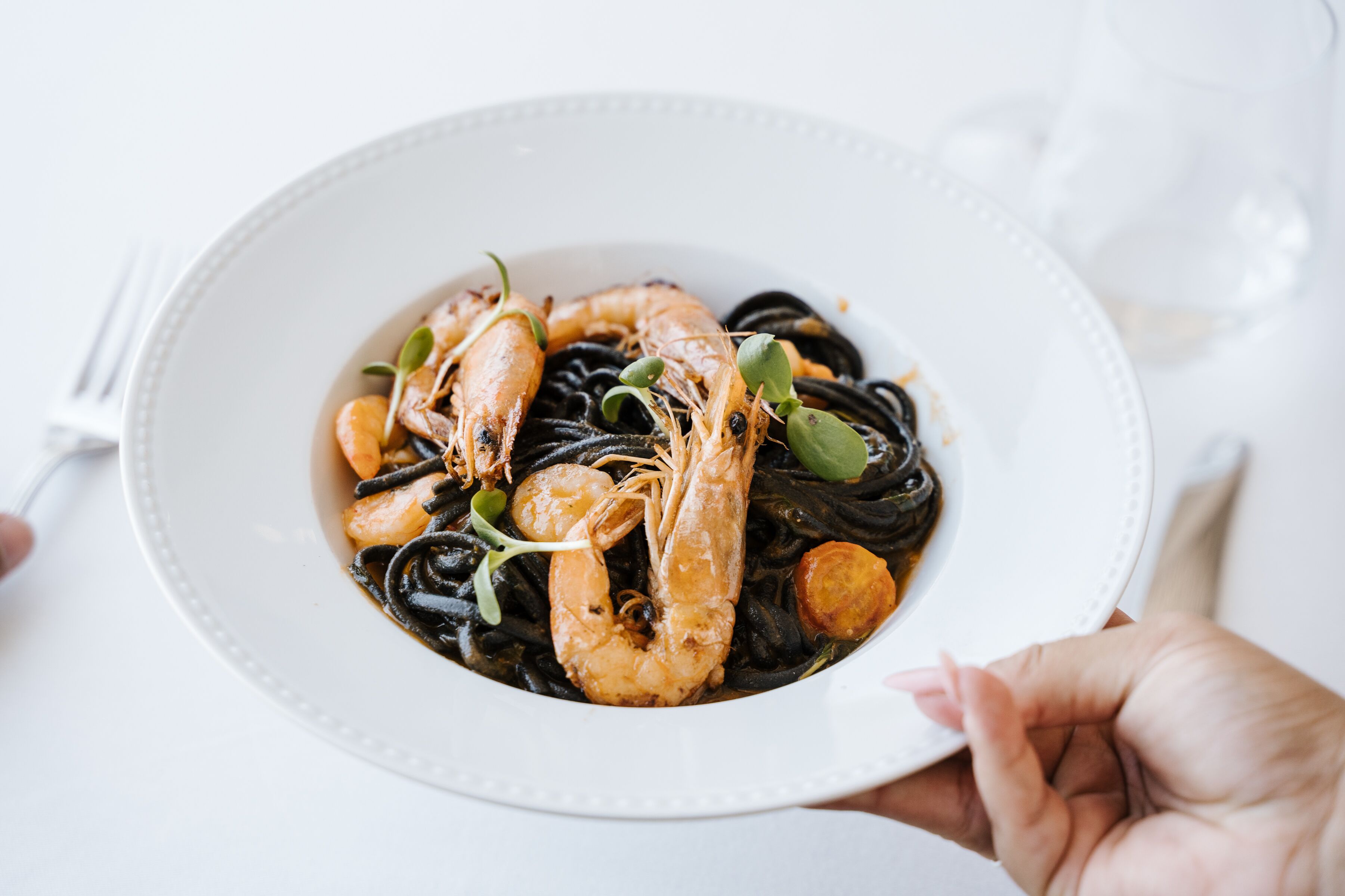 A plate of seafood pasta with shrimp and mussels, held by a hand.