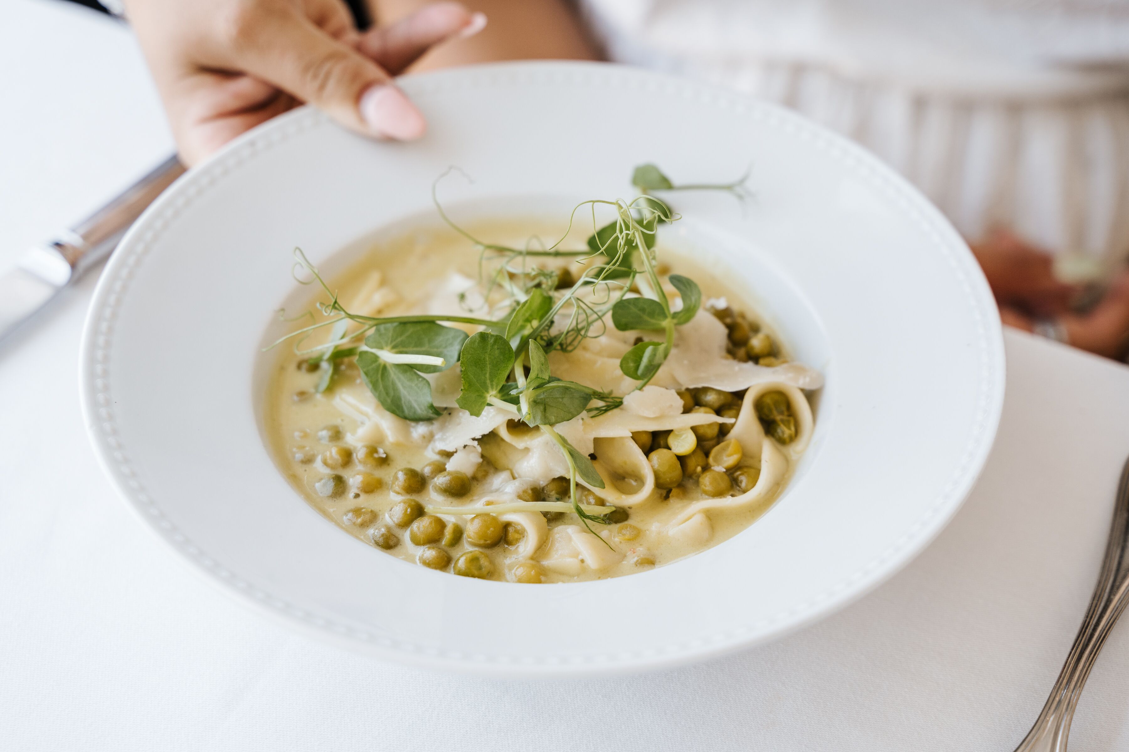 A bowl of pasta with peas and greens on a white plate.