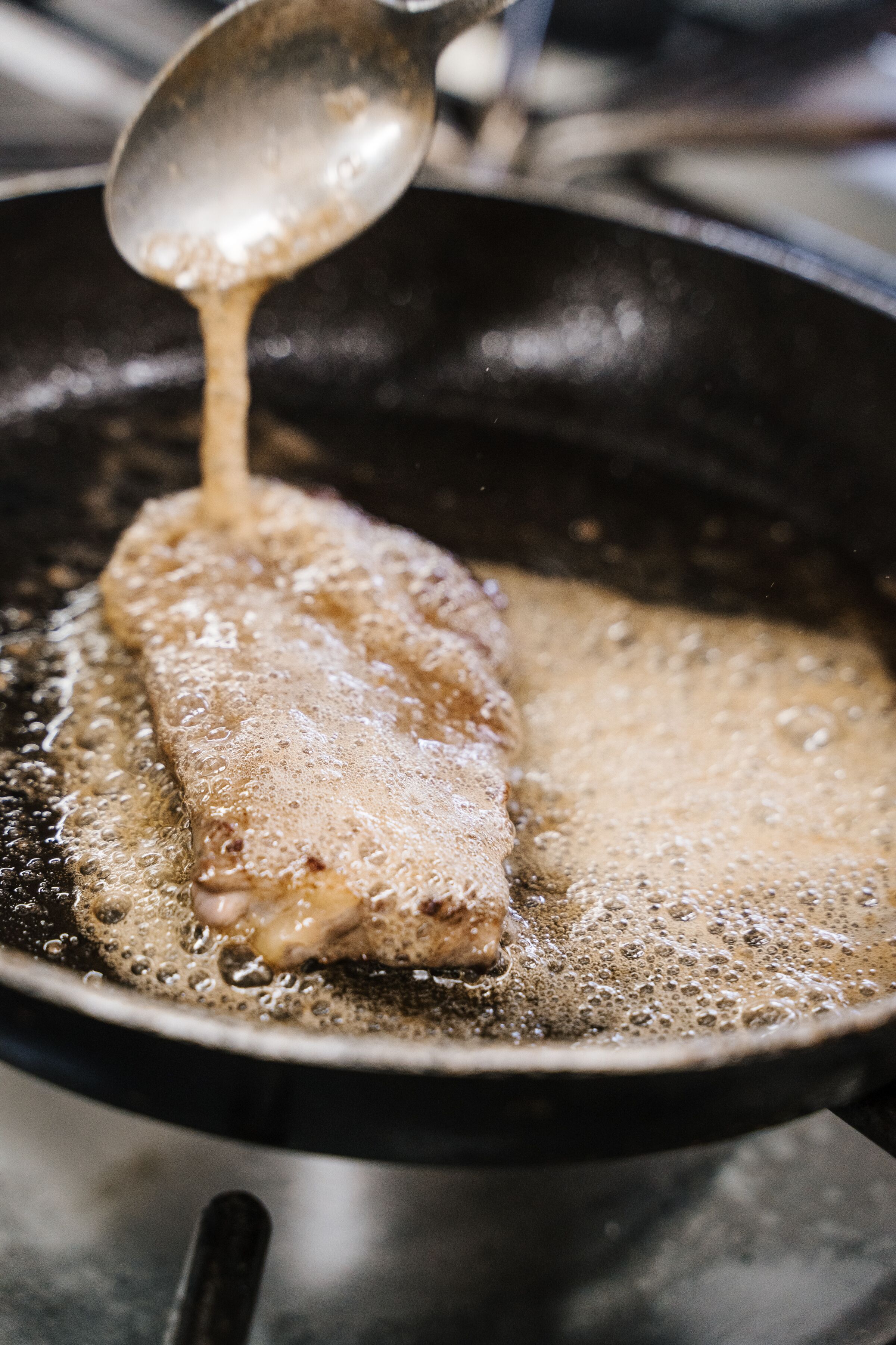 A frying pan with oil and a spoon lifting a piece of food.
