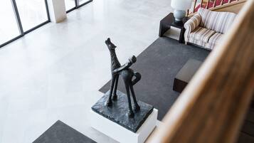 A modern interior with a sculpture on a pedestal, a sofa, and a lamp on a side table.