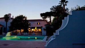 Une piscine, avec un bâtiment en arrière-plan, entourée d’arbres et sous un ciel dégagé.