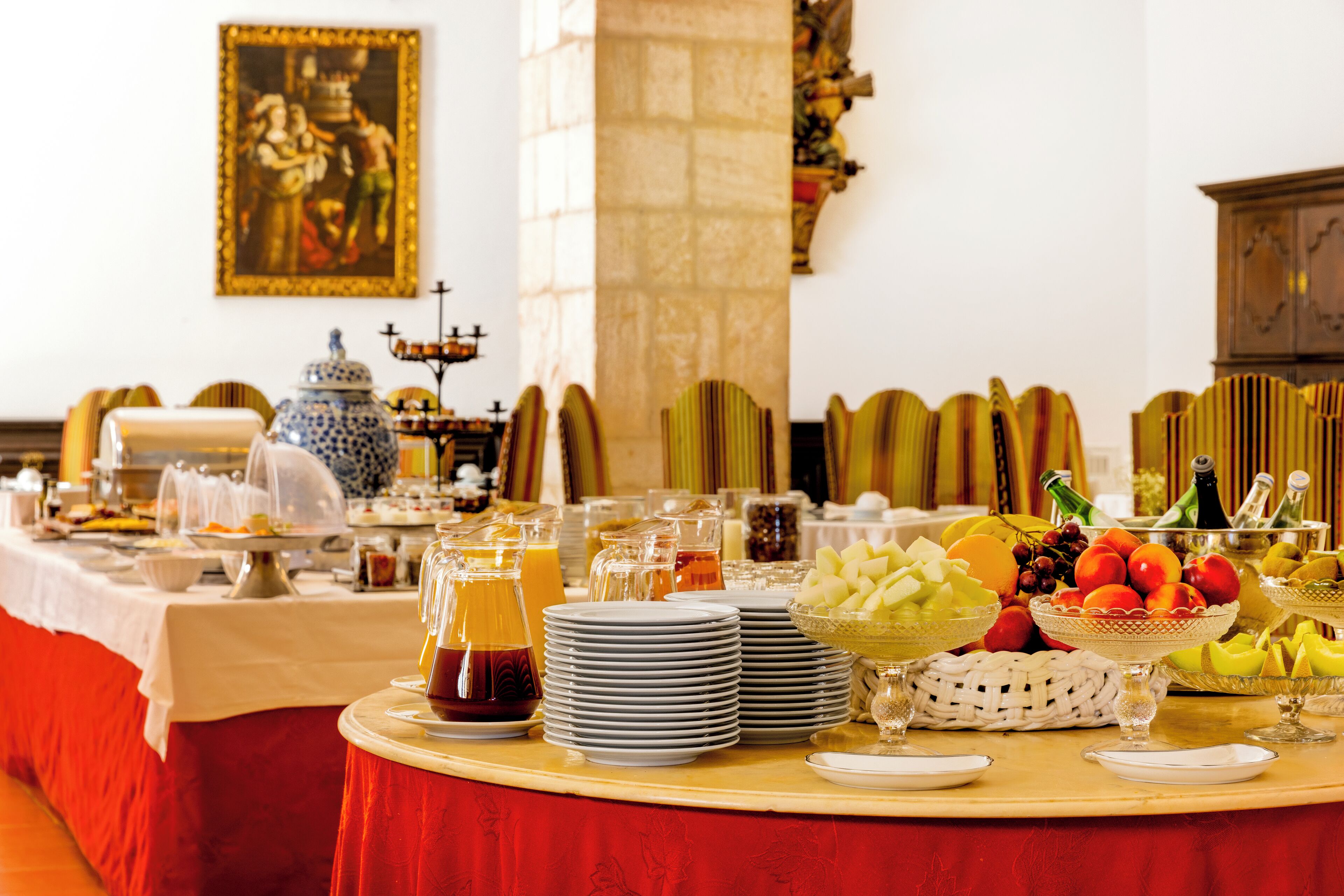 Una mesa de buffet con diversos alimentos y bebidas, rodeada de sillas y un adorno en la pared.