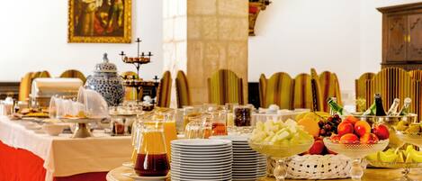 Una mesa de buffet con diversos alimentos y bebidas, rodeada de sillas y un adorno en la pared.