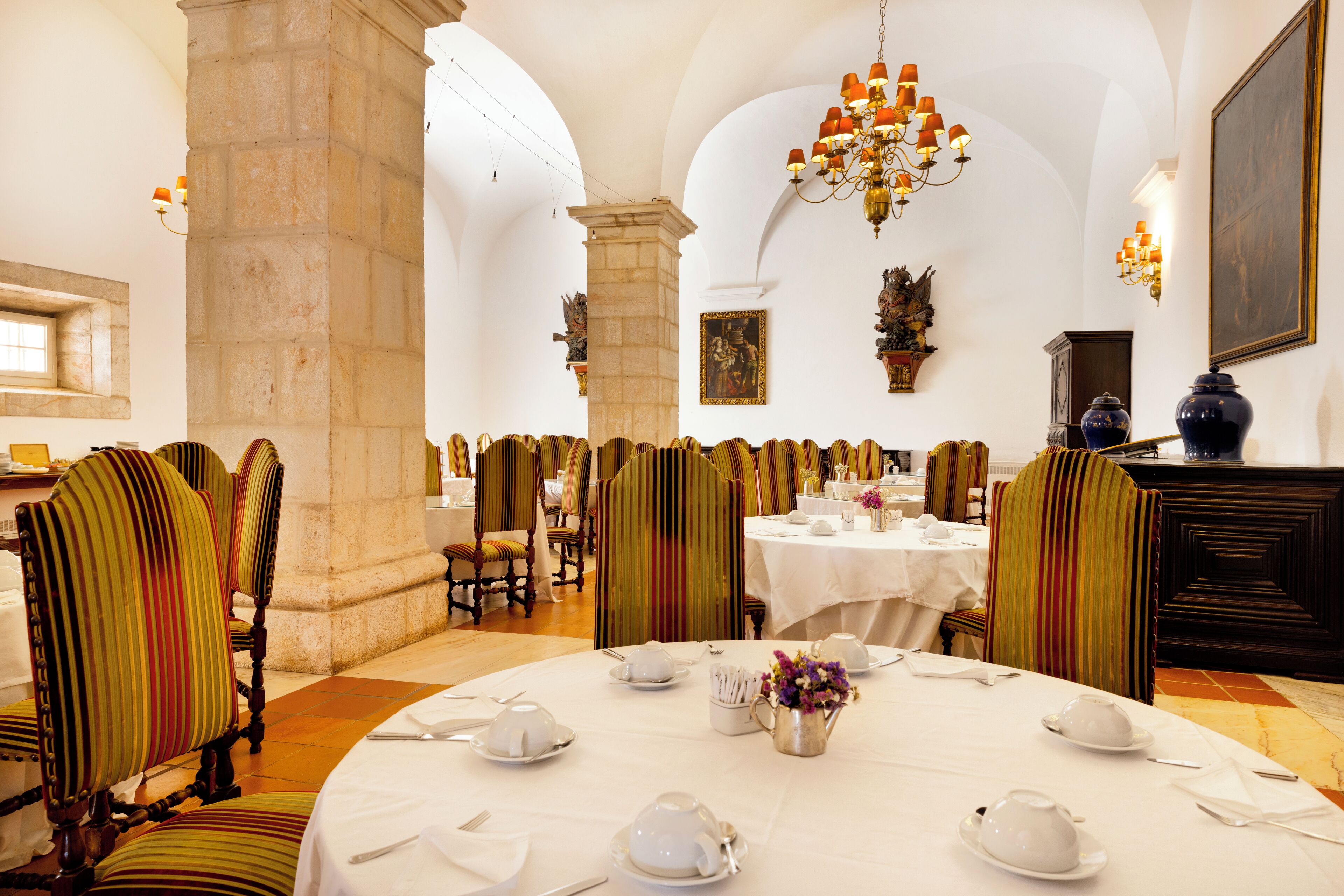 Un espace repas avec des tables rondes dressées pour le service, des chaises à motifs rayés et un lustre.