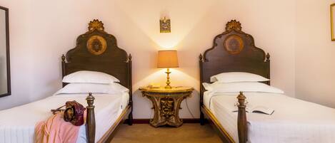 A hotel room with two wooden beds, a small table with a lamp, and a framed picture on the wall.