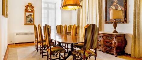 A formal dining room with a large round table, upholstered chairs, a chandelier, a classic dresser, and a framed painting.