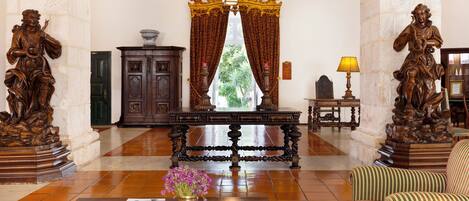 A lobby with a wooden coffee table, a vase with flowers, a wooden cabinet, a lamp, and two statues.